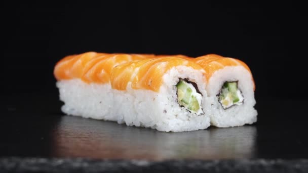 Rolki sushi obracają się na czarnym tle. Zdjęcia z bliska. Filadelfijski ser, ogórek i łosoś w japońskiej żywności. - Materiał filmowy, wideo