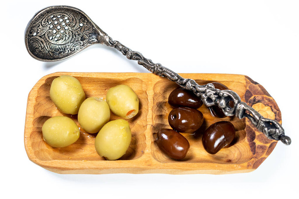 Olives noires et vertes dans un petit bol en bois, une cuillère pour les olives sur fond de surface blanche - Photo, image