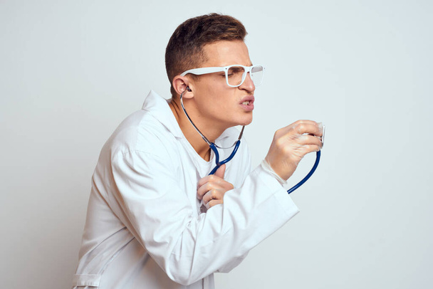 doctor in a medical gown with a stethoscope and glasses on a light background cropped view portrait - 写真・画像