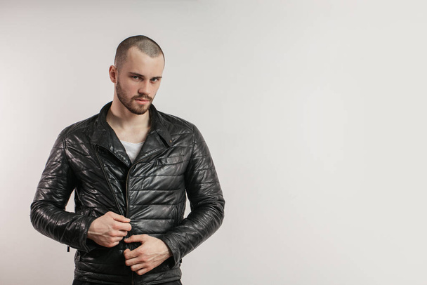 Serious attractive young man zipping up his black leather jacket - Fotografie, Obrázek