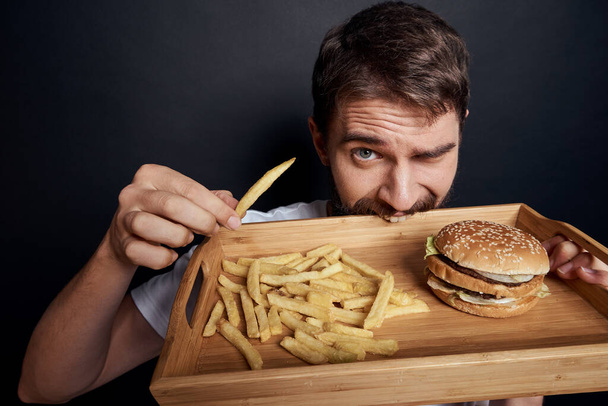 érzelmi férfi fa raklap gyorsétterem hamburger sült krumpli eszik élelmiszer életmód sötét háttér - Fotó, kép