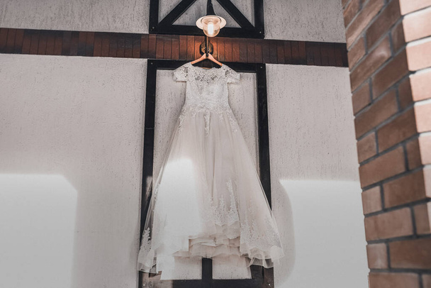 Ein weißes, luxuriöses Hochzeitskleid hängt an einem Kleiderbügel. - Foto, Bild
