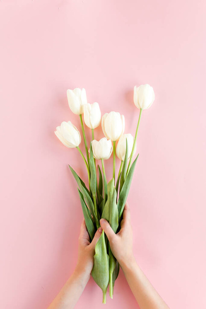 Female hands hold white tulip flowers on pink background. Minimal floral concept. Flat lay, top view. - Φωτογραφία, εικόνα