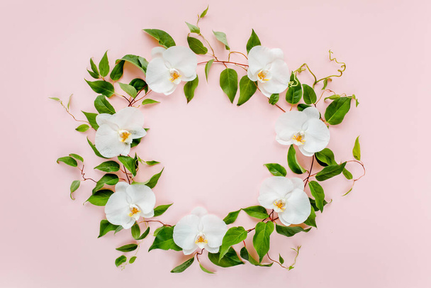 Round frame of white orchids and green leaves on a pink background. Pattern with space for your text, holiday greeting card. Flat lay, top view.  - Fotoğraf, Görsel