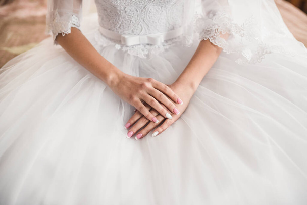 The female hands of the fair-skinned bride lie on the white wedding dress - Фото, изображение