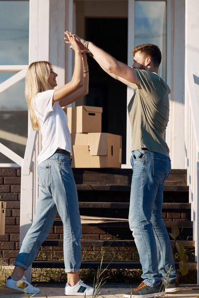 beautiful couple giving high five and smiling while standing near moving cardboard boxes outdoor - Fotoğraf, Görsel