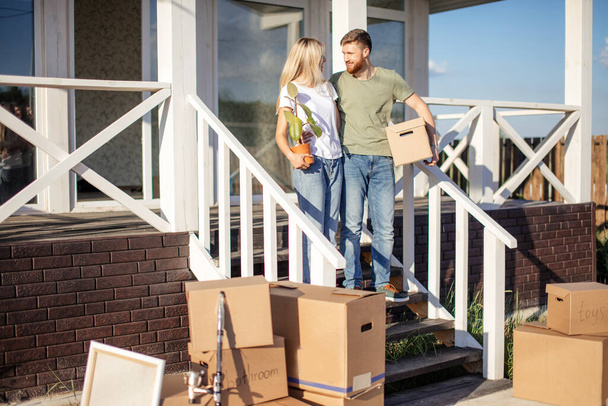 Husband and wife standing in front of new buying home with boxes - Foto, Bild