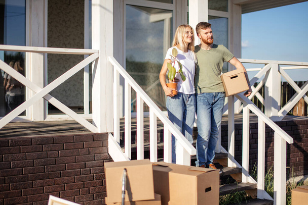 Husband and wife standing in front of new buying home with boxes - Foto, Bild