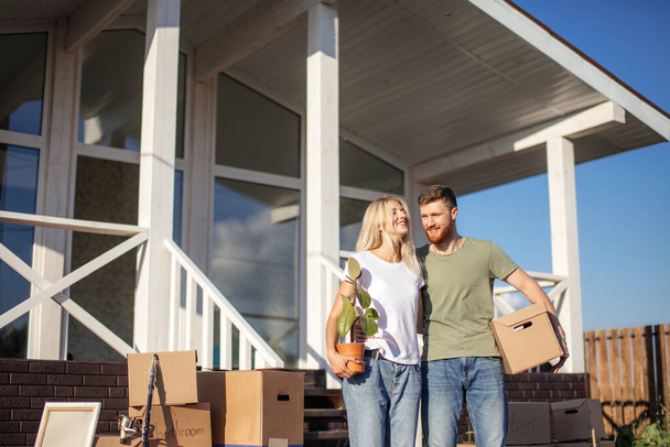 Husband and wife standing in front of new buying home with boxes - Foto, imagen