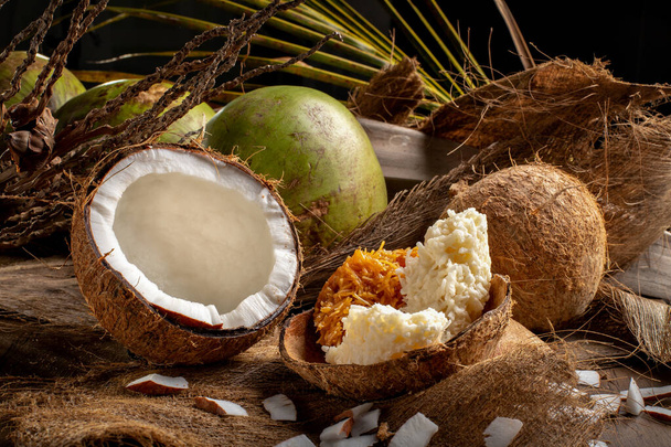 Відкрийте зелений кокос і дозрілі кокосові горіхи з солодкою кокадою (бразильською солодкою) на дерев "яному тлі і висушеним листям кокосової пальми. - Фото, зображення
