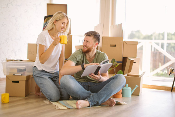 couple with book sitting on bed while moving into new home - Фото, изображение
