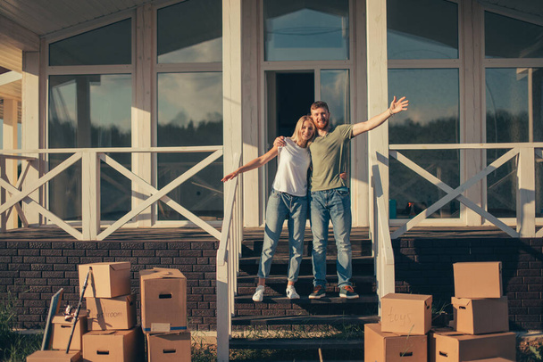 Husband and wife standing in front of new buying home with boxes - 写真・画像