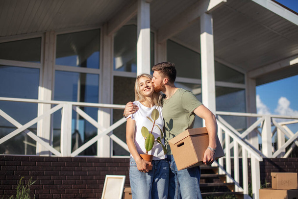 Husband and wife standing in front of new buying home with boxes - Foto, imagen
