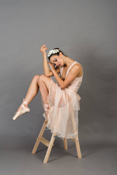 young beautiful ballet dancer in beige swimsuit posing on pointes on light grey studio background - Foto, afbeelding