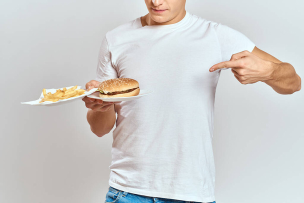 een man met frietjes en een hamburger op een lichte achtergrond in wit t-shirt close-up cropped view Copy Space Model - Foto, afbeelding