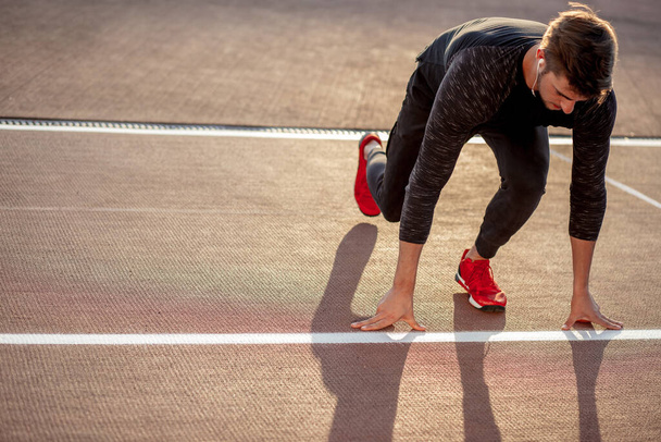 athlete on starting position at running track. Runner practicing run in stadium racetrack - Фото, изображение