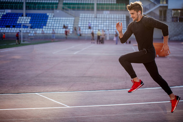 male athlete wearing black sportwear running at track, side view - Valokuva, kuva
