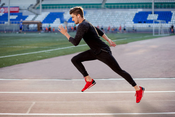 male athlete wearing black sportwear running at track, side view - Fotó, kép
