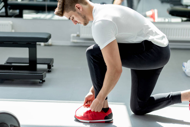 Handsome caucasian sportsman ties his red sneakers at fitness studio - Foto, Imagen