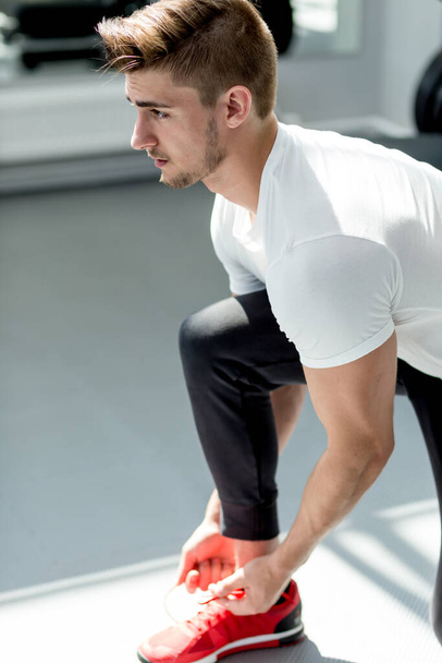 Handsome caucasian sportsman ties his red sneakers at fitness studio - Photo, Image