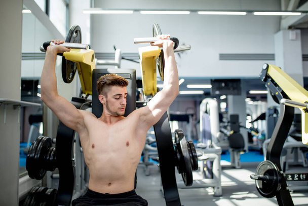 A young athlete trains in the gym. Bodybuilder pumping up upper body muscules. - Foto, imagen