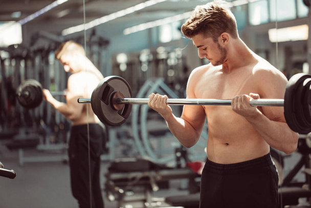 young man flexing muscles with barbell in gym - Foto, imagen