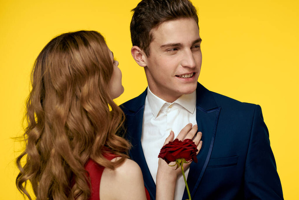 Un homme romantique étreint une femme dans une robe rouge avec une rose à la main sur un fond jaune - Photo, image