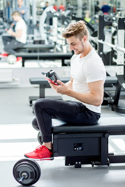 Man drinking protein shake from blender in gym while looking at camera - Fotoğraf, Görsel