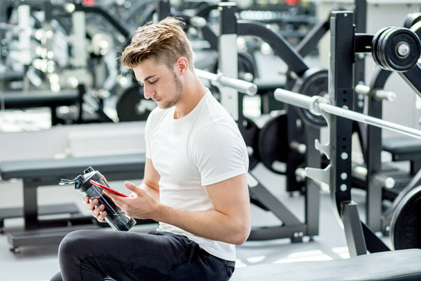 Man drinking protein shake from blender in gym while looking at camera - Foto, Bild