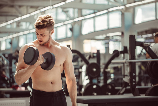 Attractive sportsman working out with dumbbells in gym - Foto, Bild