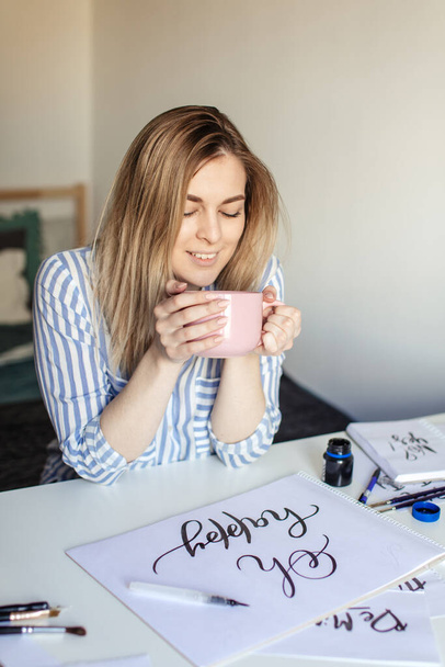 Gros plan femme écrivant de belles notes sur papier sur bureau blanc tout en buvant du café ou du thé - Photo, image