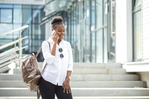 African american woman with backpack walking outdoor and talking on mobile phone - Photo, Image