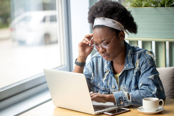 Afrikaanse vrouwelijke blogger, typt een nieuwe post tijdens de lunch in een café. - Foto, afbeelding