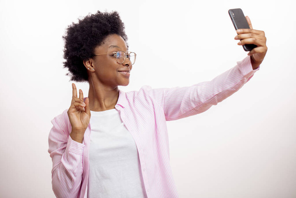 atractiva hembra afro mostrando dos dedos mientras toma una foto de sí misma. - Foto, imagen