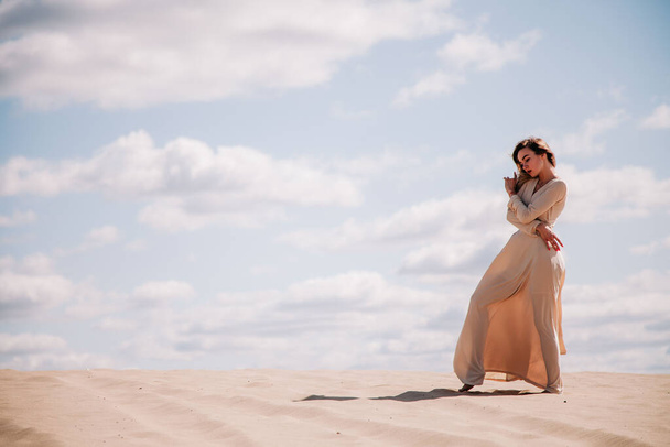 Young, slender girl in beige dress walks in the desert - Фото, зображення
