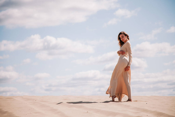 Young, slender girl in beige dress walks in the desert - Фото, зображення