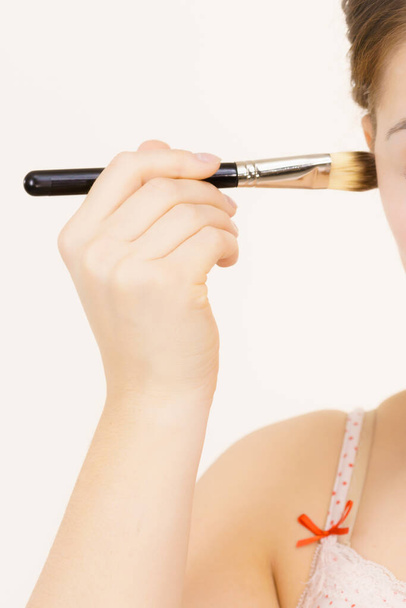 Frau hält Make-up-Pinsel bereit, um kosmetische Foundation auf ihr Gesicht aufzutragen. - Foto, Bild