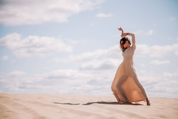 Young, slender girl in beige dress walks in the desert - Фото, изображение