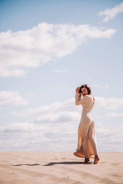 Young, slender girl in beige dress walks in the desert - 写真・画像