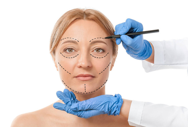 白い背景に女性の顔にマークを適用する形成外科医 - 写真・画像
