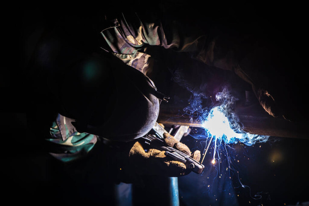 Welder at work. Man in a protective mask. The welder makes seams on the metal. Sparks and smoke when welding. - Photo, Image