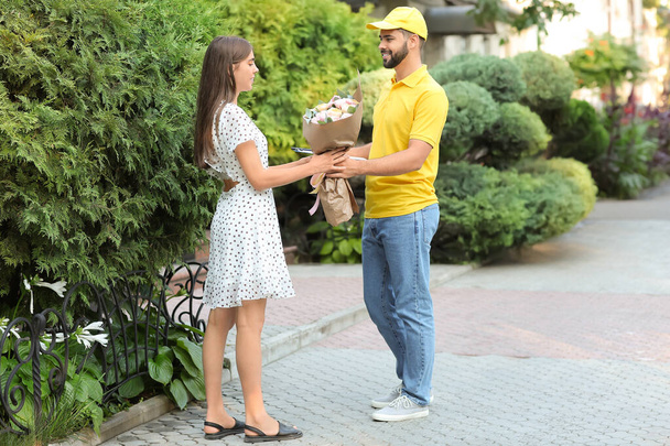 Young woman receiving bouquet of flowers from courier outdoors - Foto, Bild