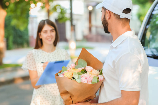 Young woman receiving bouquet of flowers from courier outdoors - Photo, Image