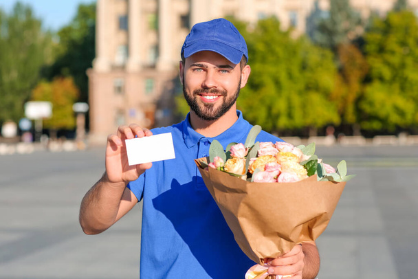 Delivery man with bouquet of beautiful flowers and blank business card outdoors - Fotoğraf, Görsel