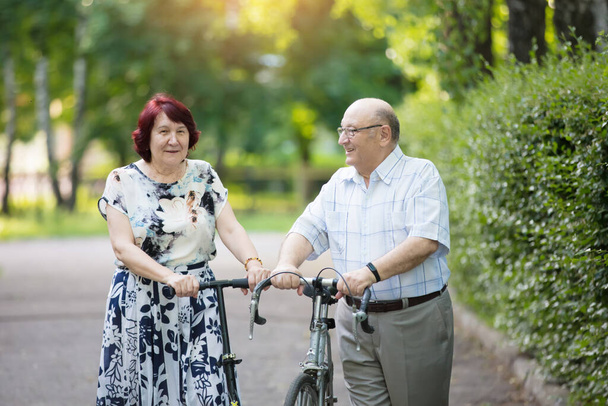 Boldog idős pár biciklivel. Jóképű férfi és nő idős polgárok. Férj és feleség idős korban sétálni. - Fotó, kép