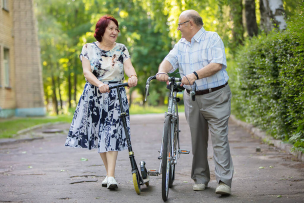 Happy elderly couple with a bicycle. Handsome man and woman senior citizens. Husband and wife of old age in the park. - Photo, Image