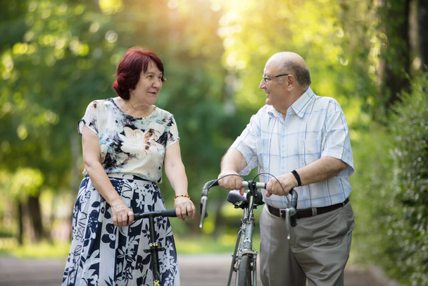 Happy elderly couple with a bicycle. Handsome man and woman senior citizens. Husband and wife of old age for a walk. - Photo, Image