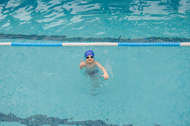 Вид сверху улыбающегося 7-летнего мальчика, играющего и плавающего в бассейне - Фото, изображение