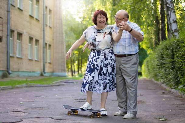 Счастливая пожилая пара со скейтбордом. Красивый мужчина и женщина пожилые люди. Муж и жена преклонного возраста для прогулки по городу. - Фото, изображение