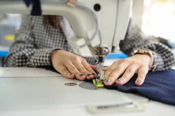 κοντινό πλάνο φωτογραφία των χεριών μιας νεαρής γυναίκας ράψιμο με ραπτομηχανή σε ένα εργοστάσιο - Φωτογραφία, εικόνα
